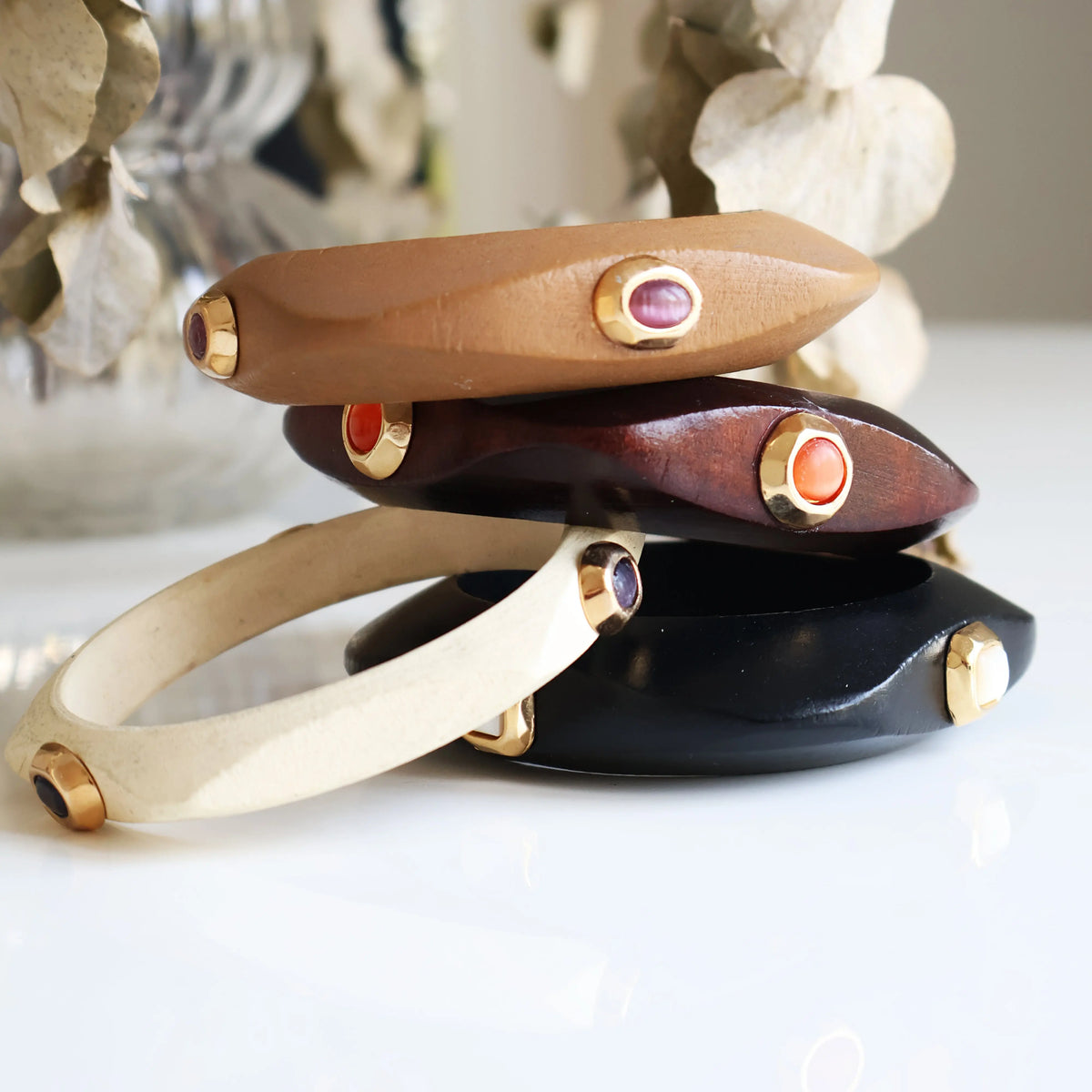 Brazaletes elegantes de cuero marrón, negro, blanco y madera con detalles en metal dorado y piedras de colores.