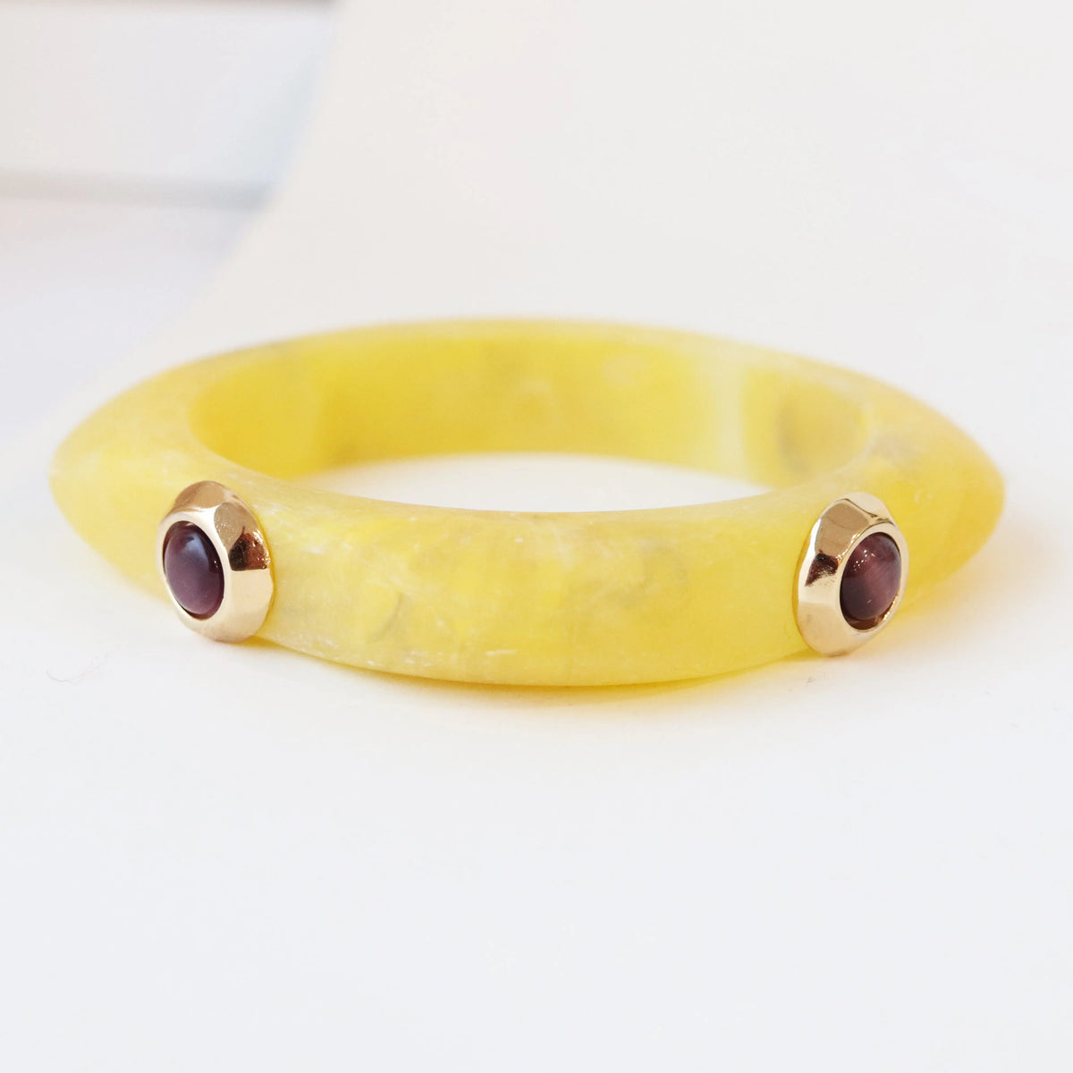 Pulsera de resina amarilla con detalles dorados y gemas moradas. Estilo moderno y elegante.