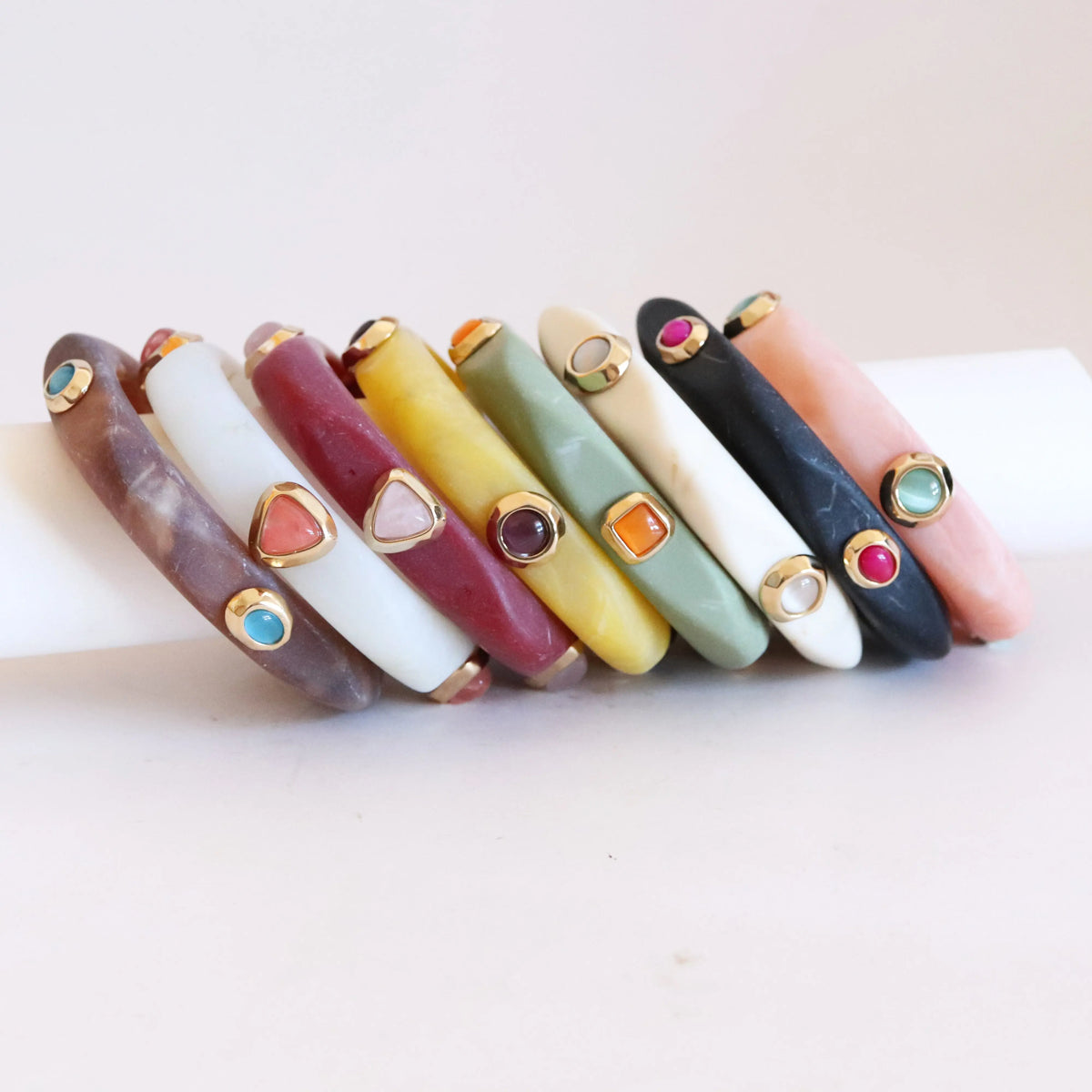 Pulseras de resina en tonos variados con detalles dorados y piedras preciosas, estilo moderno y colorido.