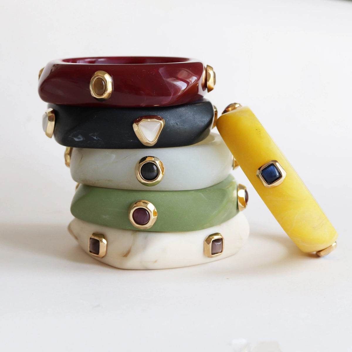 Pulseras apiladas en tonos rojo, negro, gris, verde, amarillo y blanco, con detalles dorados y piedras decorativas.