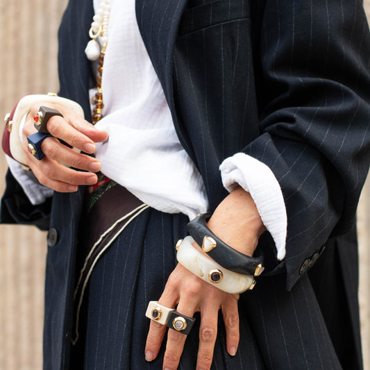 Conjunto de pulseras negras y blancas con detalles dorados, estilo elegante y moderno, sobre chaqueta a rayas.