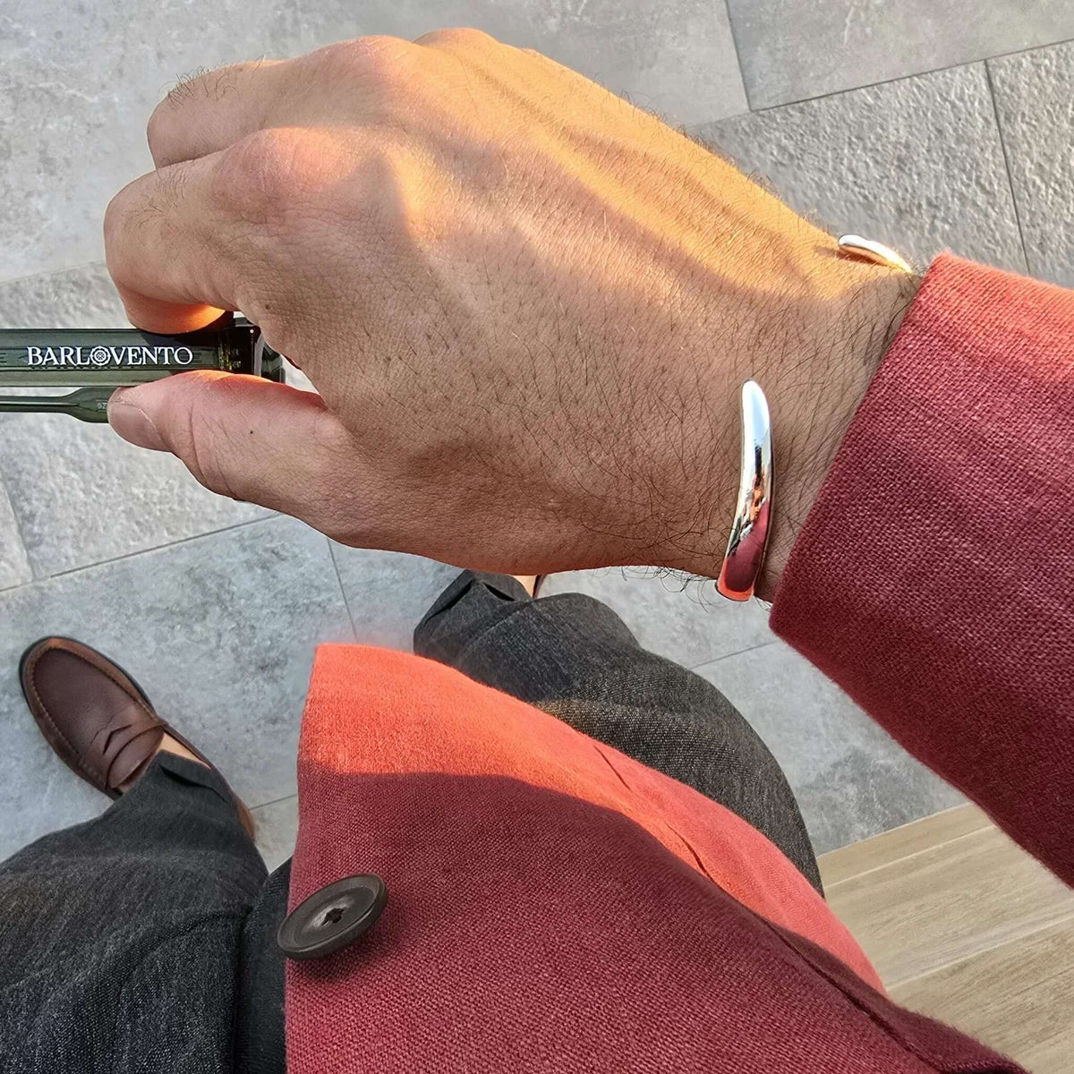 Mano sosteniendo gafas de sol con montura verde y lentes oscuras, usando un brazalete metálico plateado.