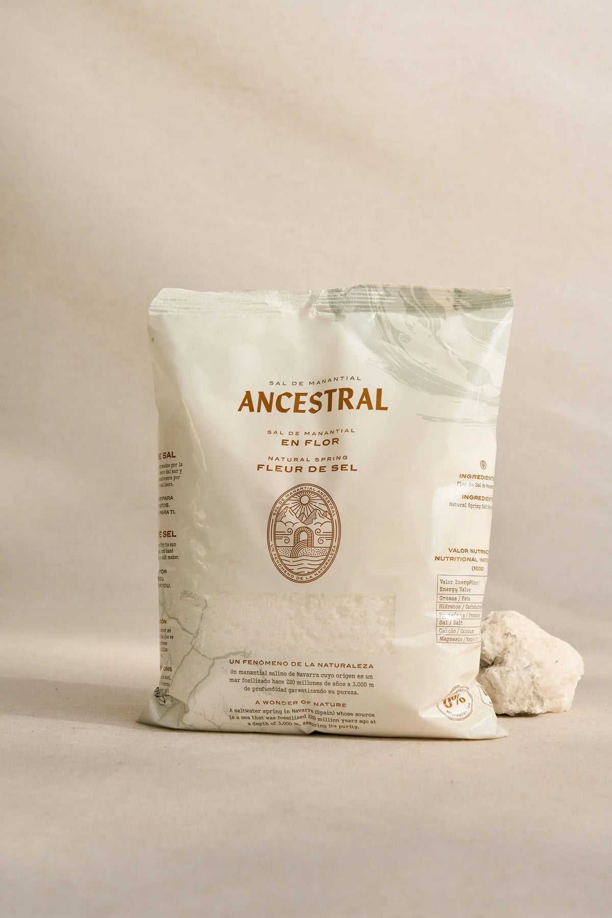 Off-white bag of Ancestral gourmet spring salt with brown text and an emblem, next to a textured white rock.
