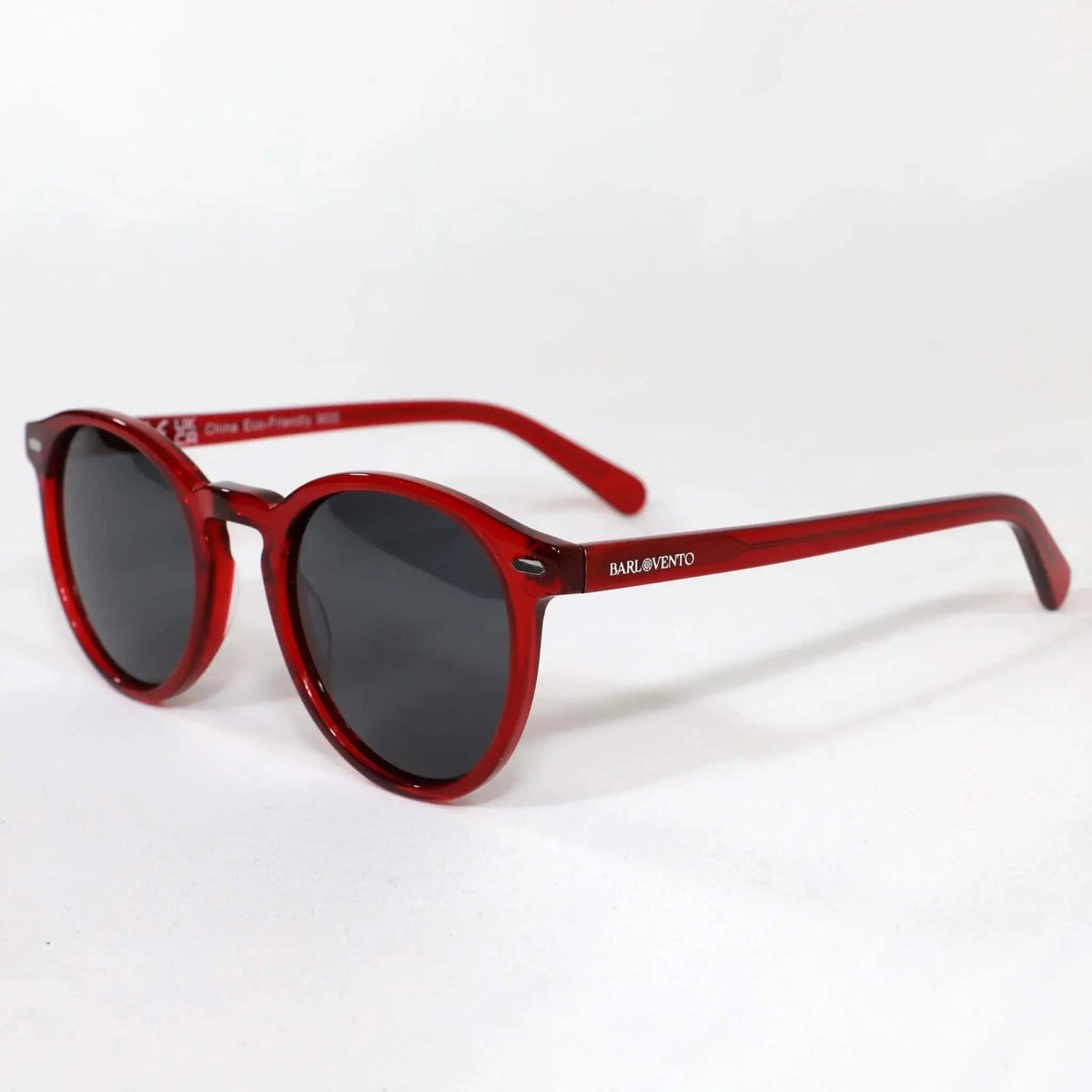 Gafas de sol redondas con montura de acetato rojo translúcido y cristales oscuros sobre fondo blanco.
