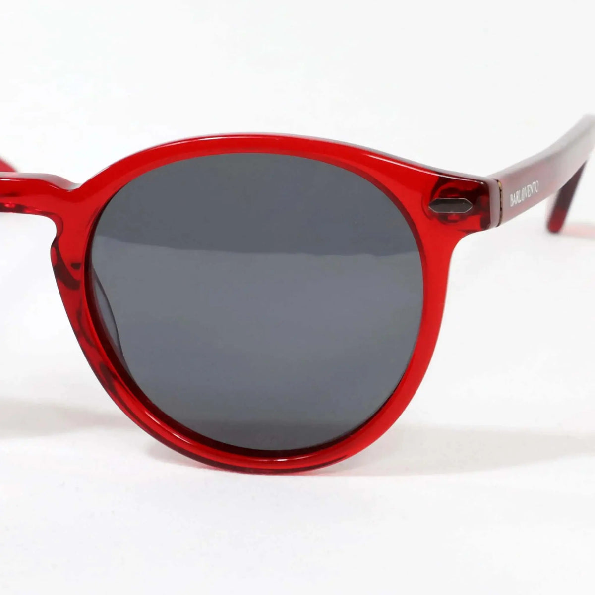 Gafas de sol de montura redonda en acetato rojo translúcido con cristales oscuros y acabado brillante.