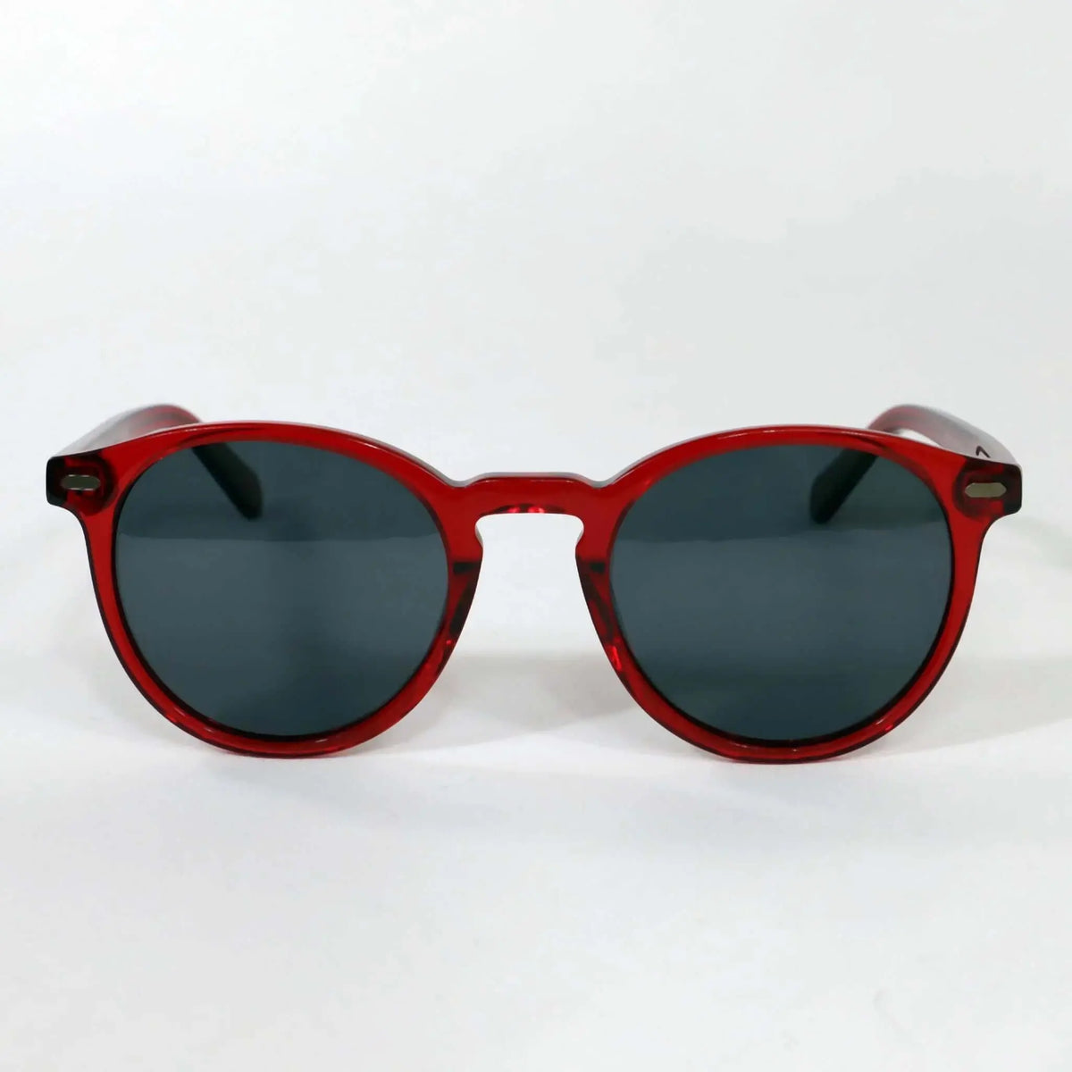 Gafas de sol redondas con montura de acetato rojo translúcido y cristales oscuros sobre fondo blanco.