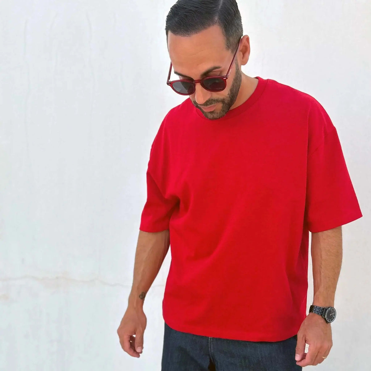 Hombre con camiseta roja y gafas de sol redondas de montura y cristal rojo sobre fondo blanco.