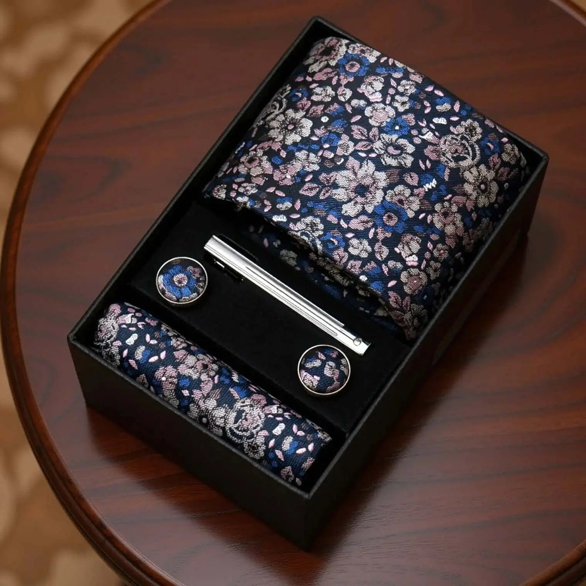 Set de corbata, pañuelo y gemelos con estampado floral en tonos azul y rosa, incluye pisacorbata metálico en caja.
