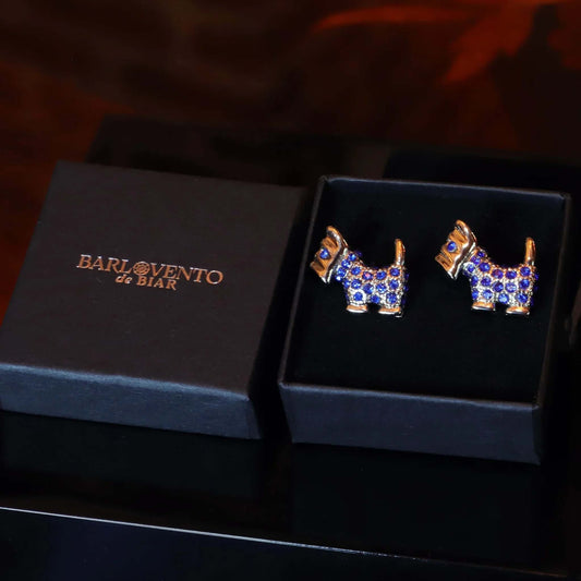 Gemelos plateados con forma de perro Terrier escocés, incrustados con brillantes gemas azules en una caja negra.