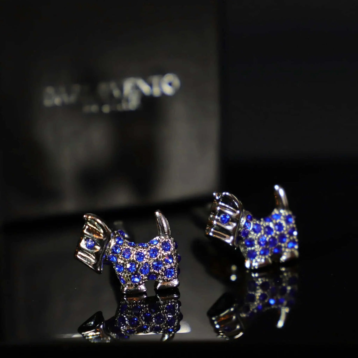 Gemelos plateados con forma de perro Terrier, adornados con brillantes cristales azules sobre fondo oscuro.