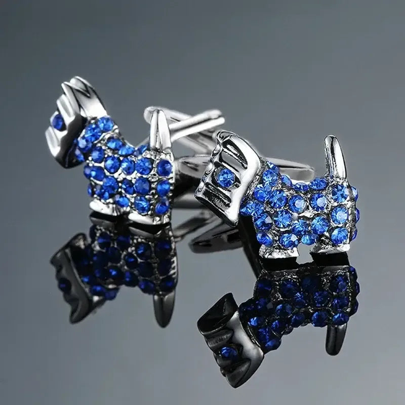 Gemelos plateados con forma de perro terrier, decorados con brillantes cristales azules sobre fondo gris reflejado.