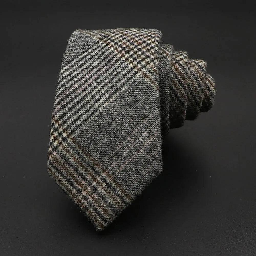 Corbata de lana gris con estampado de cuadros estilo tweed, textura tejida y acabado elegante sobre fondo negro.