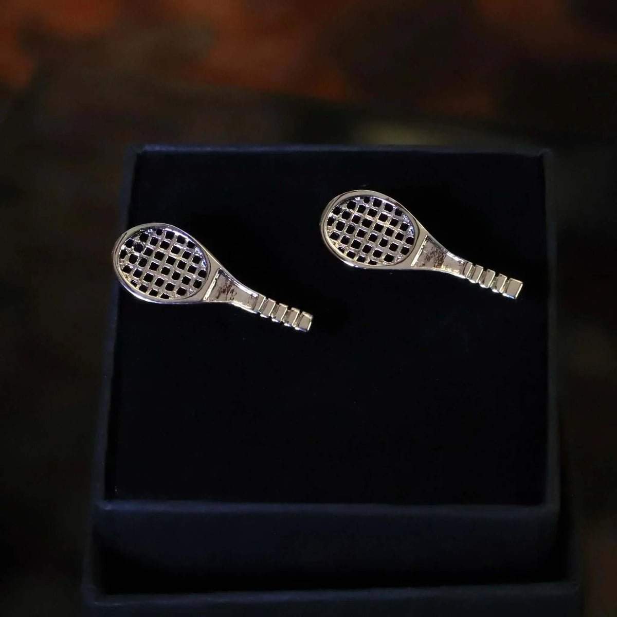 Gemelos de camisa plateados con forma de raqueta de tenis, acabado metálico brillante en estuche negro de regalo.