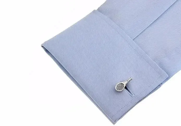 Gemelo metálico plateado con forma de raqueta de tenis en el puño de una camisa de vestir azul claro.