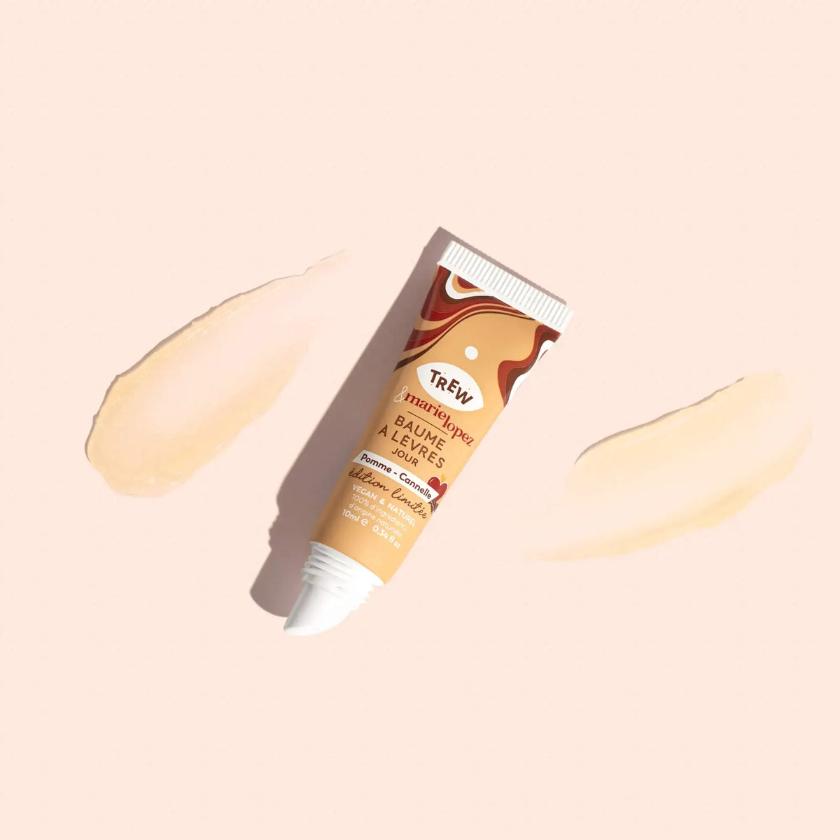 Lip balm tube with swirl design, labeled "Pomme Cannelle," centered between two sheer product swatches on beige.