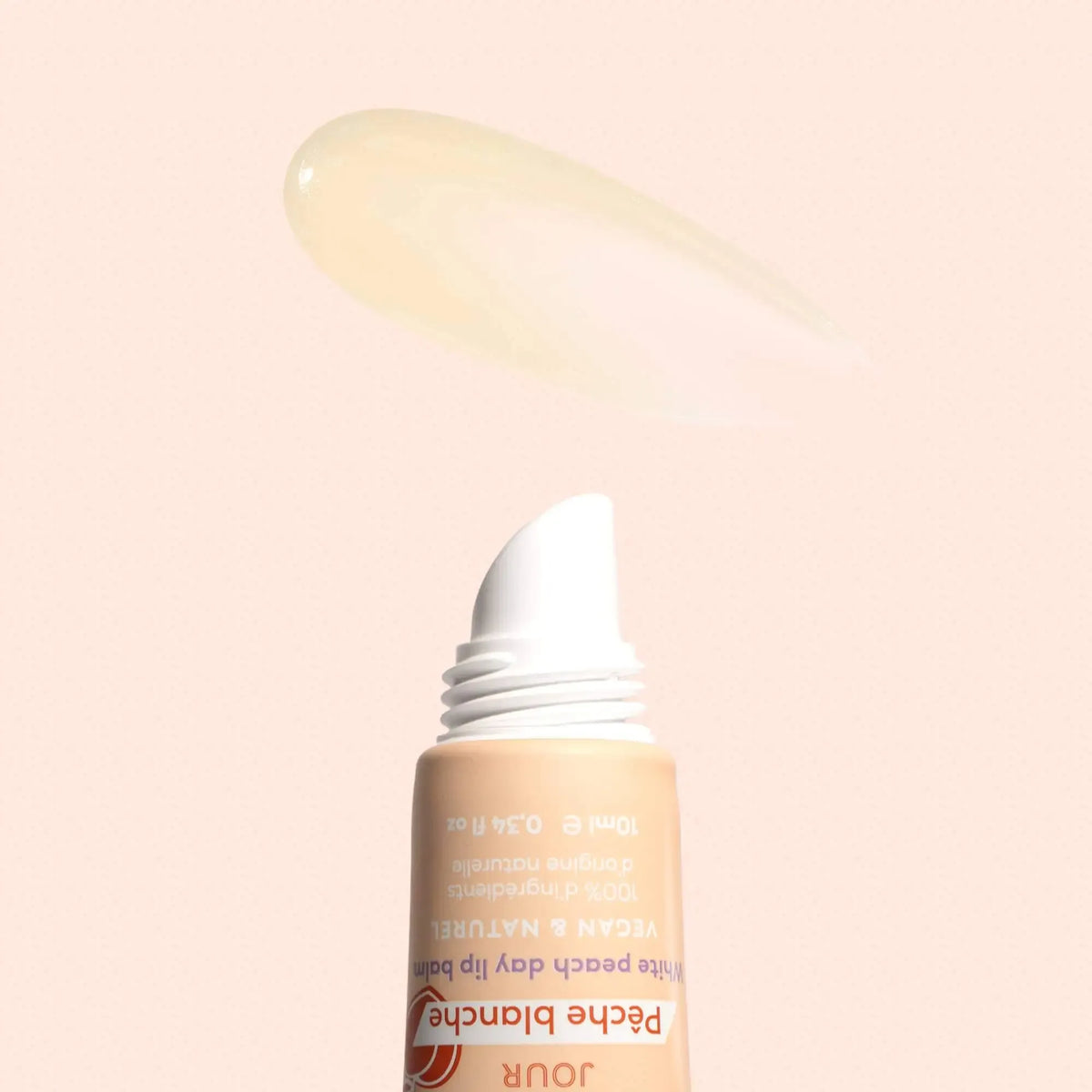 Squeeze tube of white peach lip balm with a smear of clear, glossy product above it on a soft peach background.