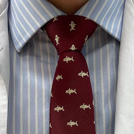 Corbata de diseño en color burdeos con estampado de pequeños tiburones beige sobre camisa de rayas azul y blanca.