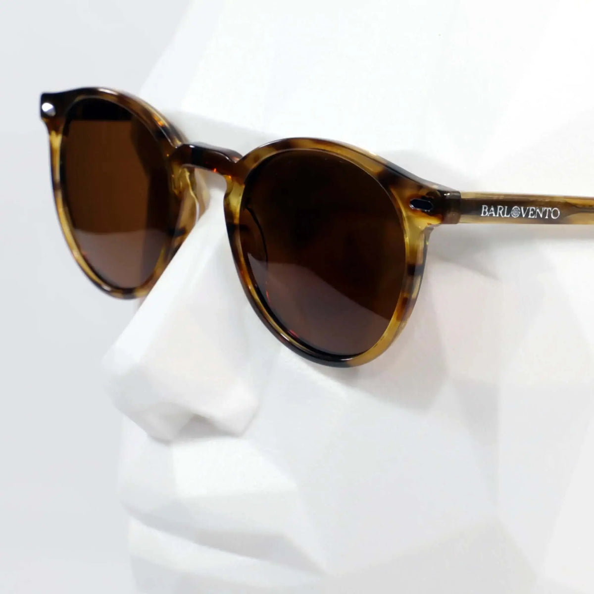 Gafas de sol redondas con montura estilo carey color naranja cristal y lentes marrones sobre maniquí blanco.