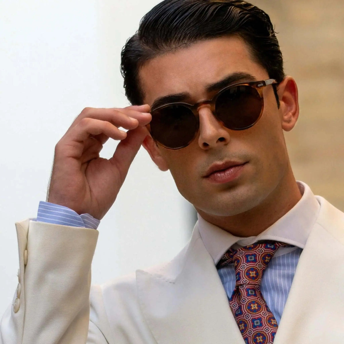 Hombre con gafas de sol redondas de acetato naranja cristal y lentes marrones, vistiendo traje y corbata elegante.