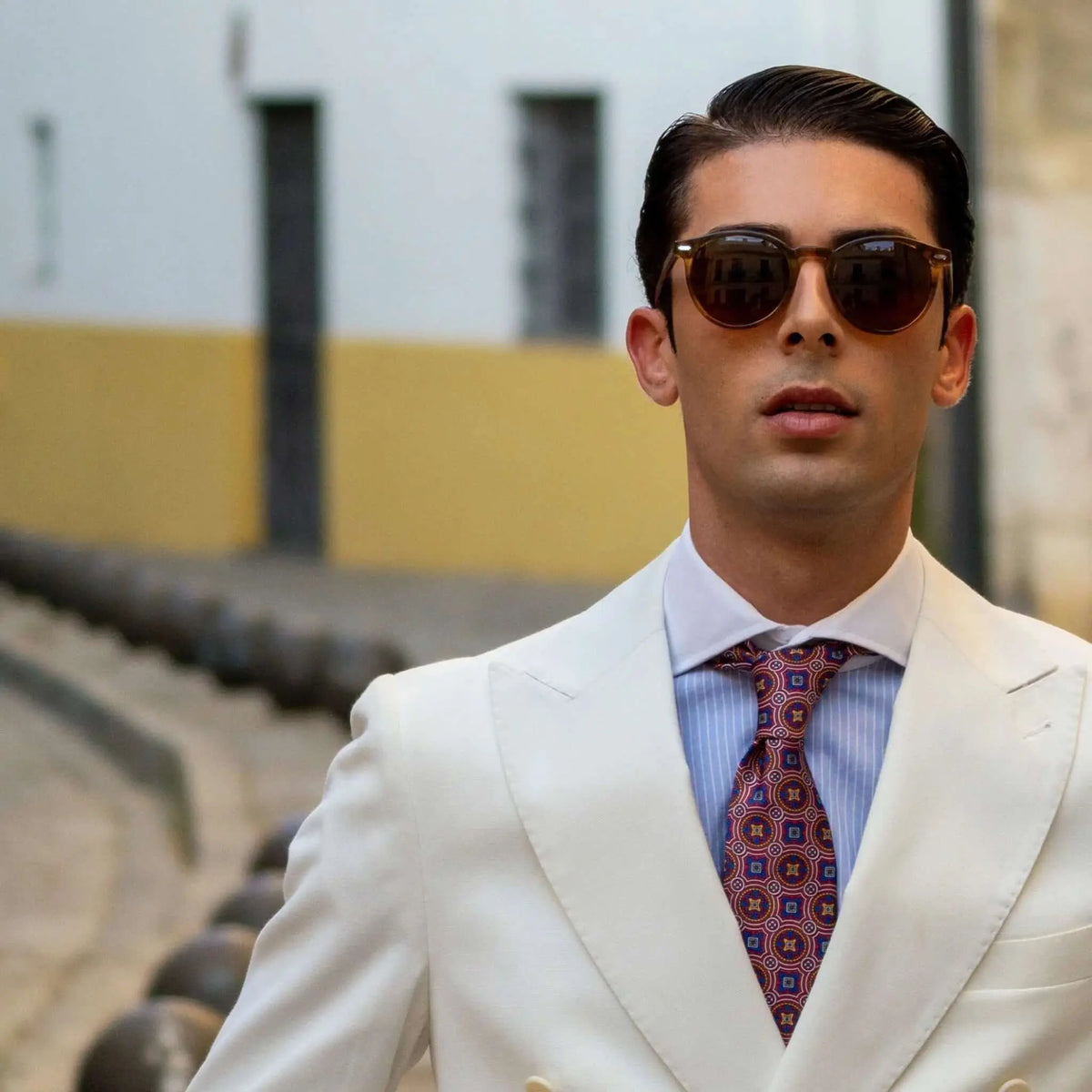 Hombre con traje blanco y gafas de sol redondas de acetato naranja cristal con lentes marrones oscuras.