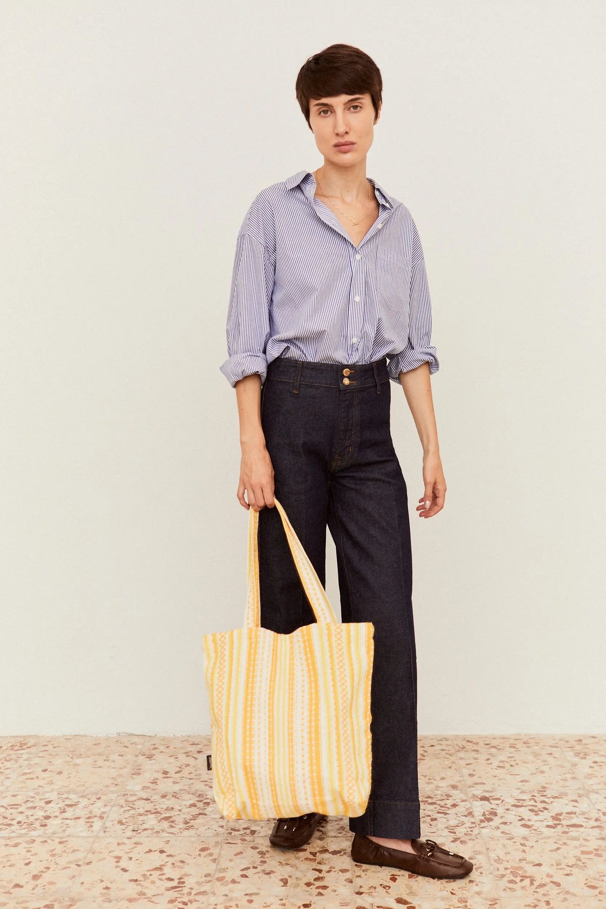 Tote bag de tela con estampado a rayas verticales en tonos amarillos y blancos de estilo artesanal y textura textil.