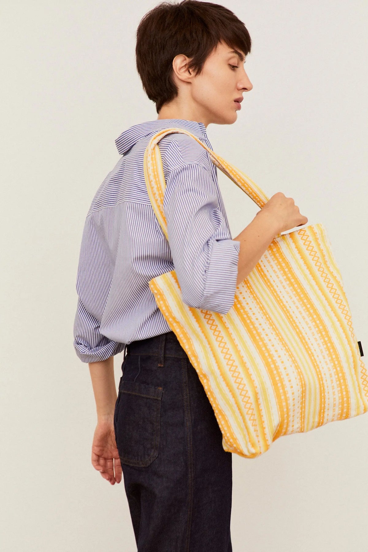 Tote bag de tela estilo alpujarra con rayas verticales en tonos amarillos y blancos, colgada al hombro.