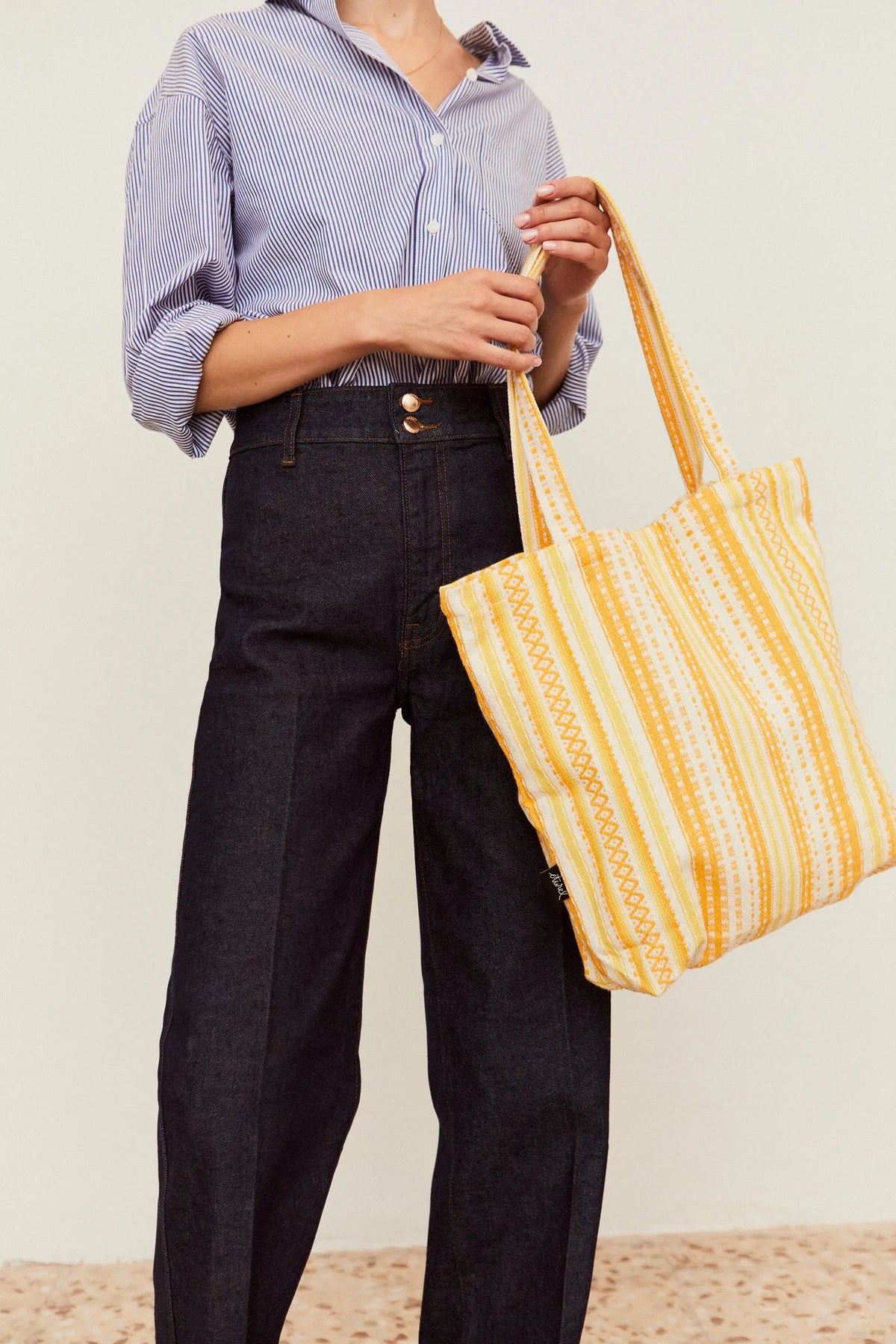 Yellow and white striped fabric tote bag with an intricate woven geometric pattern, held by a person in a shirt.