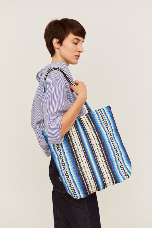 Tote bag de tela estilo alpujarra con estampado de rayas azules, blancas y negras, colgada al hombro por una modelo.
