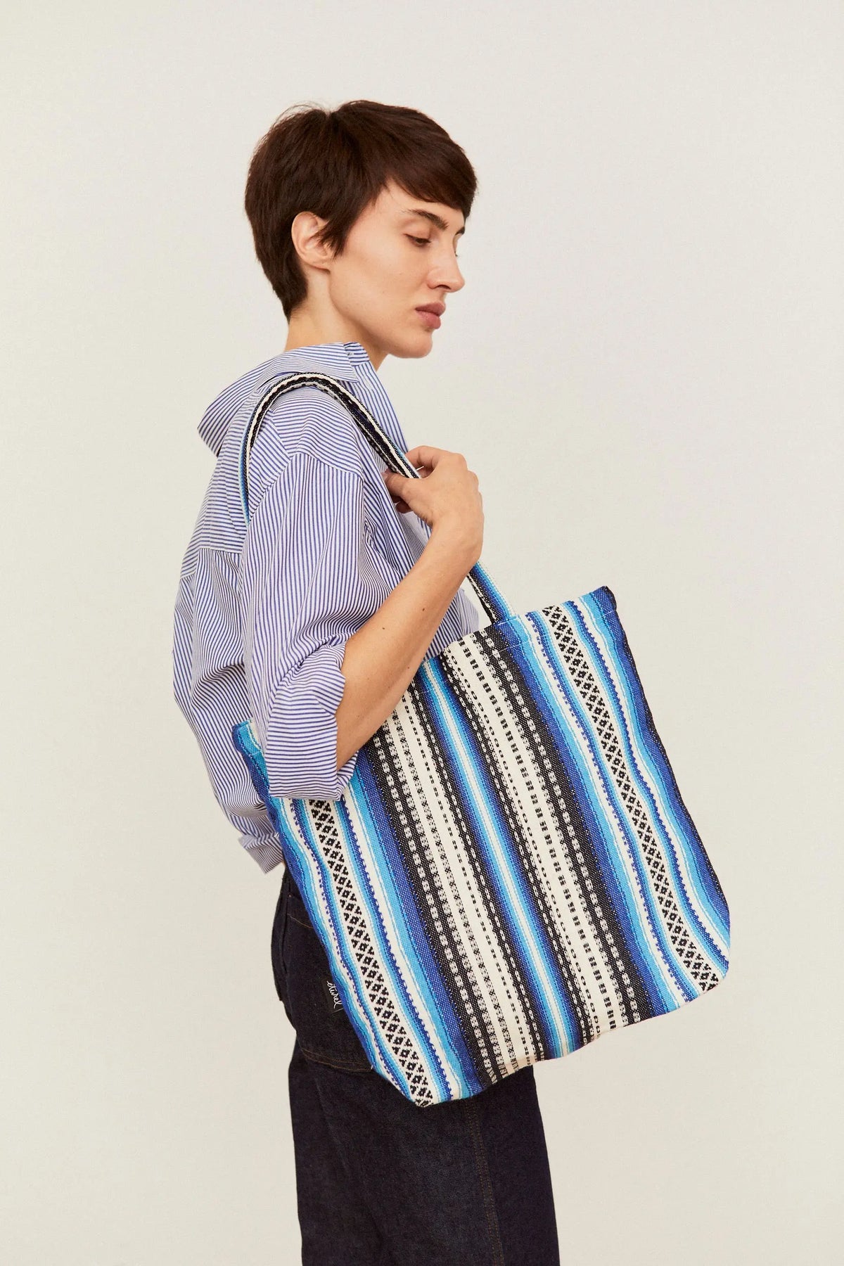 Tote bag de tela estilo alpujarra con estampado de rayas azules, blancas y negras, colgada al hombro por una modelo.