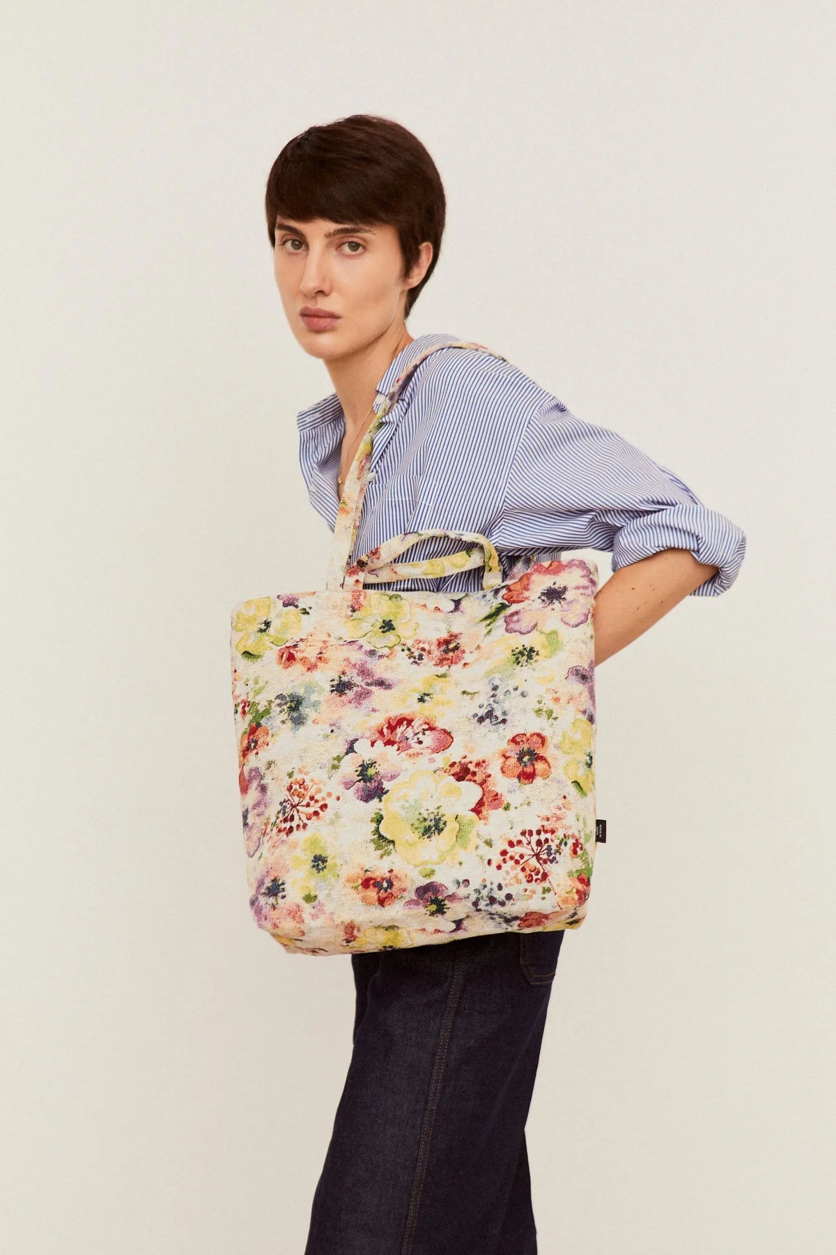 Tote bag de tejido jacquard con estampado floral multicolor de amapolas, colgado al hombro de una modelo.