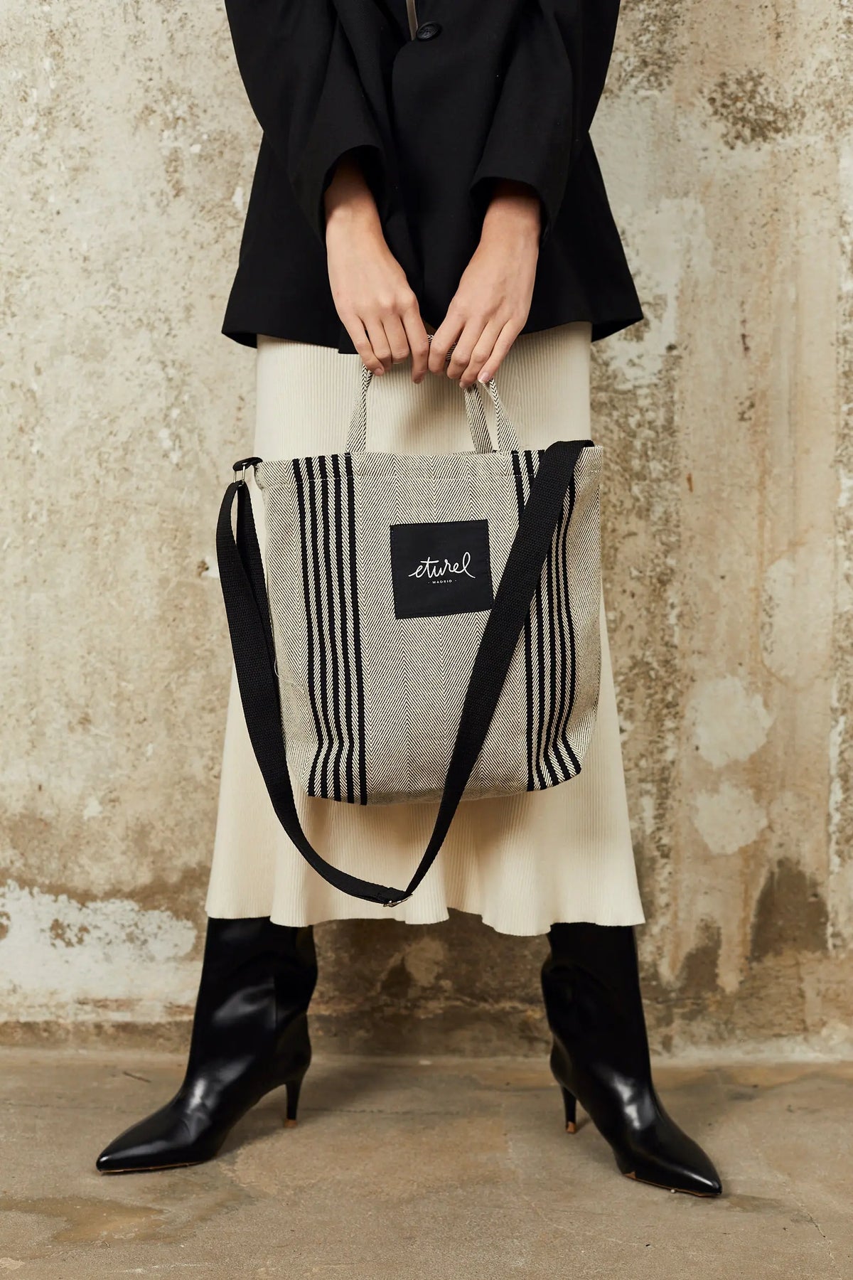 Black and cream striped twill tote bag with top handles, a black crossbody strap, and a square brand logo patch.