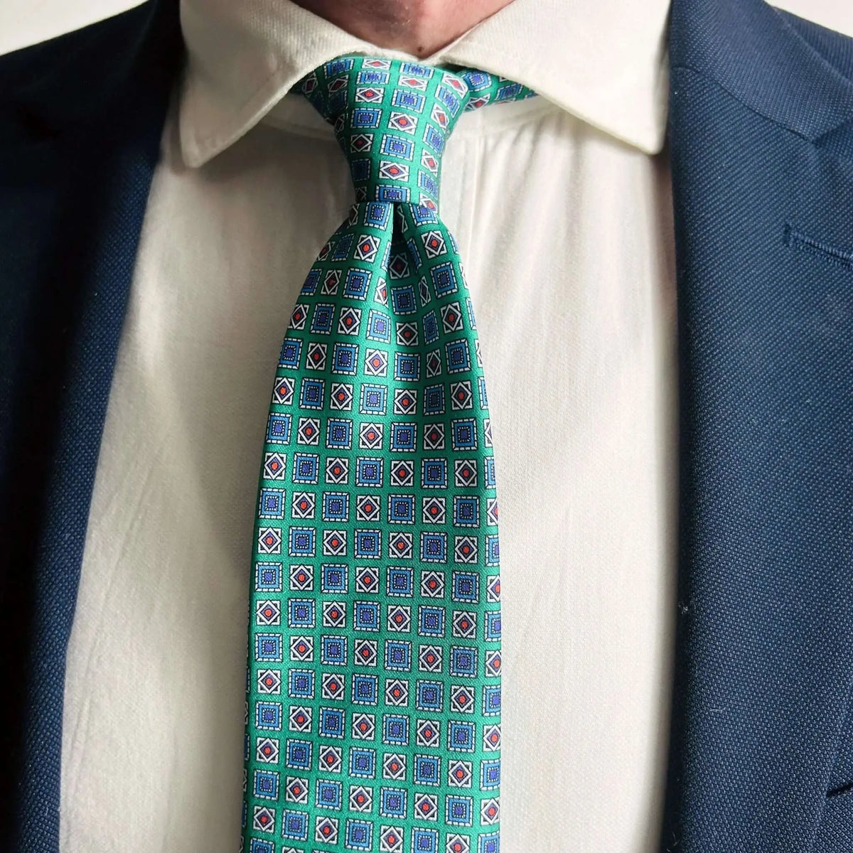 Corbata verde de seda con estampado geométrico y rombos, combinada con camisa blanca y americana azul marino.
