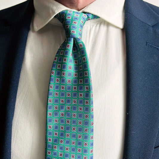 Corbata verde de seda con estampado geométrico y rombos, combinada con camisa blanca y americana azul marino.