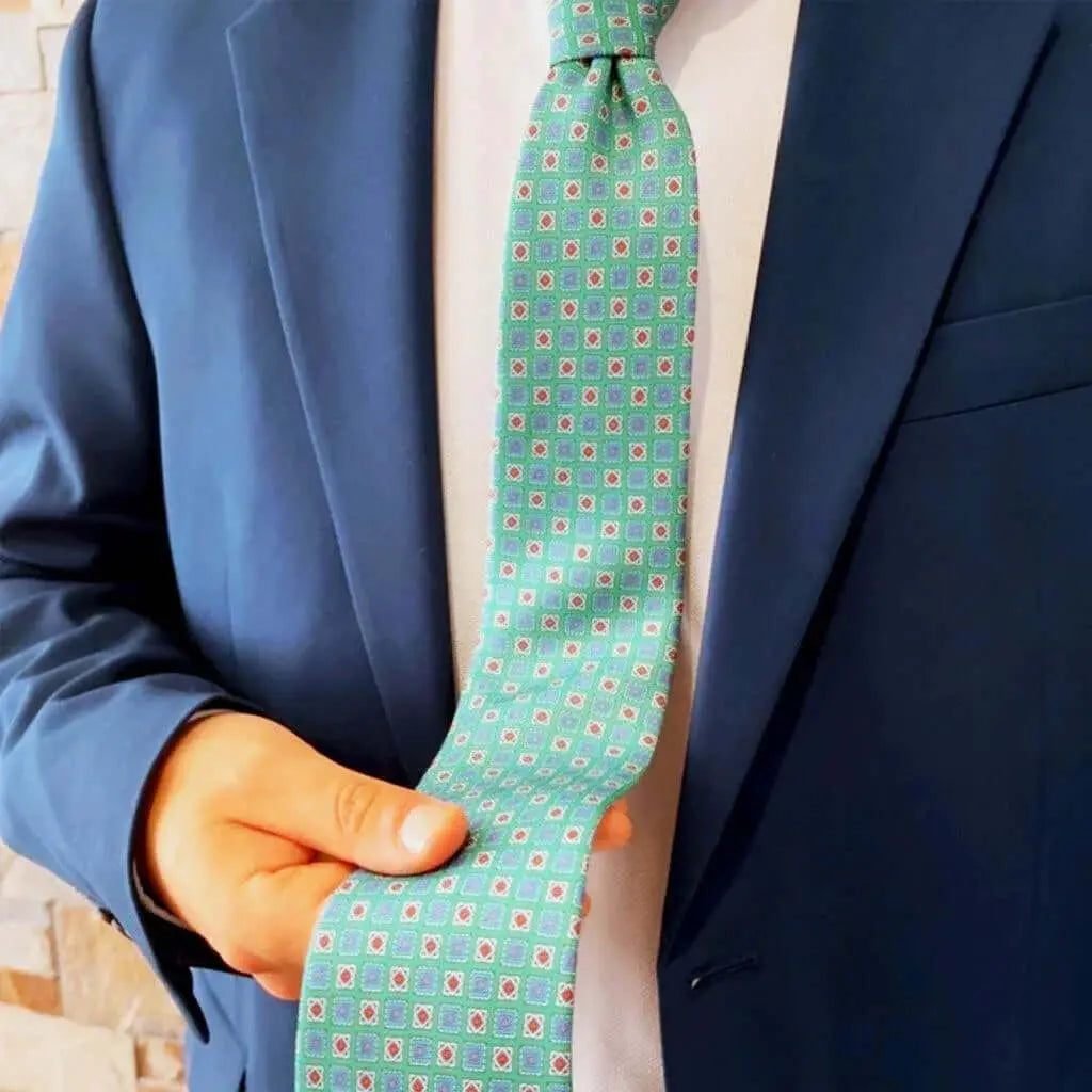 Corbata verde con estampado geométrico de pequeños cuadros sobre americana azul y camisa blanca. Estilo formal italiano.