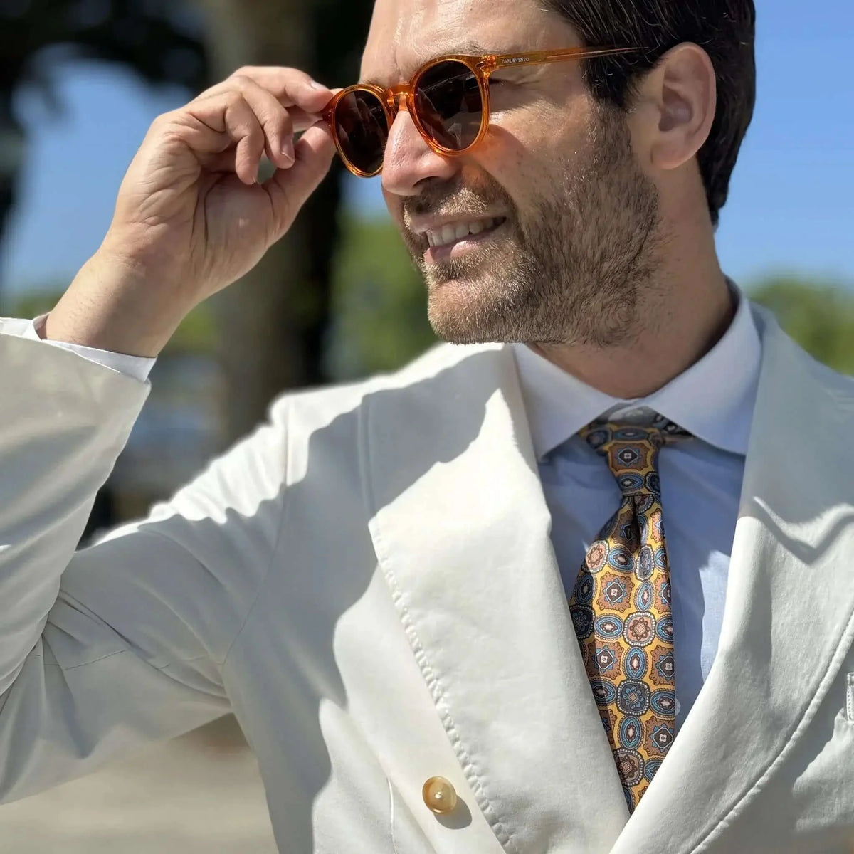 Hombre con traje blanco y gafas de sol redondas de acetato naranja transparente estilo retro y cristales oscuros.
