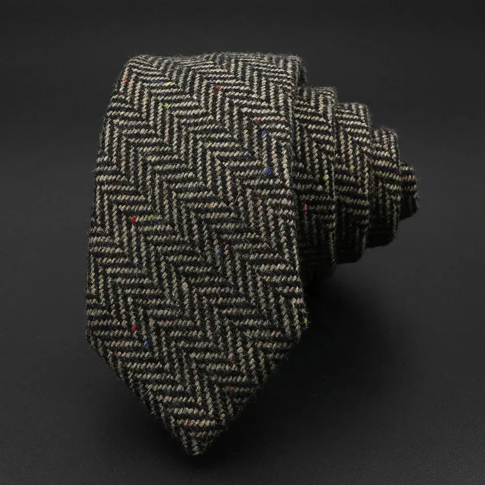 Corbata de lana gris con tejido de espiga y sutiles motas de colores, enrollada sobre un fondo negro.
