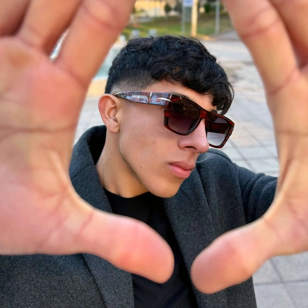 Joven con abrigo gris y gafas de sol rectangulares estilo carey con lentes degradadas, marco moderno y acabado brillante.