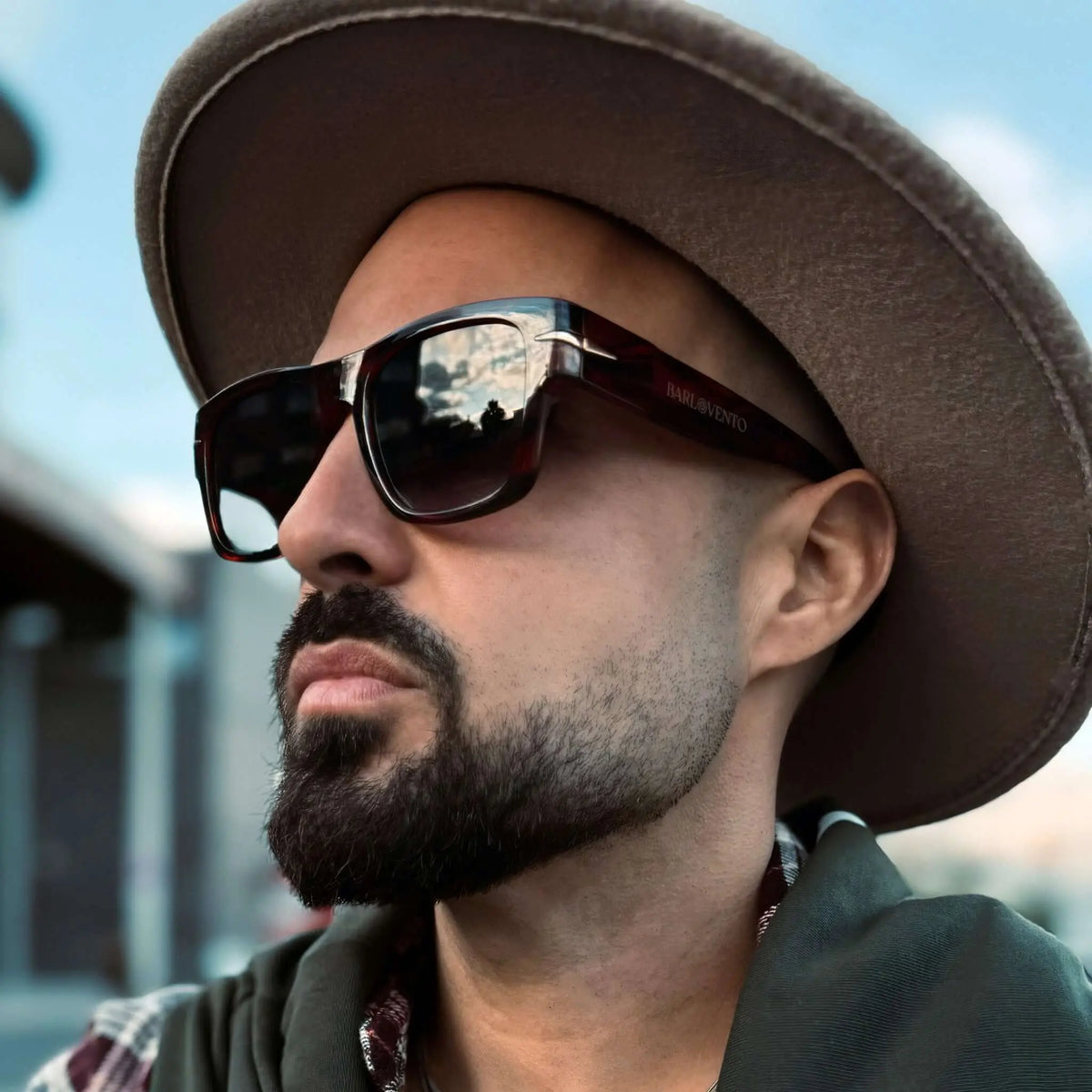Hombre con barba y sombrero lleva gafas de sol de carey con montura cuadrada y cristales oscuros con filtro UV400.