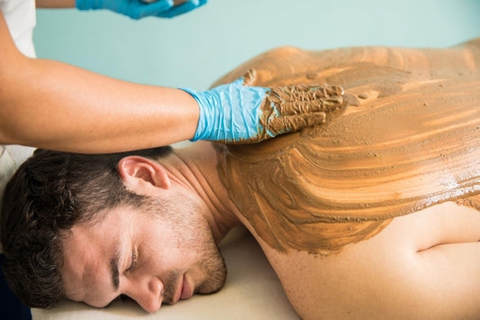 Peel-Off Body Wrap at Home therapist applying mud clay mask on man's back