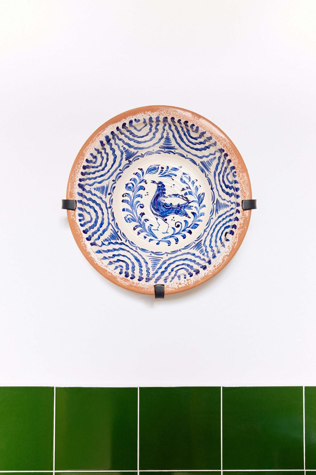 Soporte de pared de hierro negro sosteniendo un lebrillo de cerámica decorado con motivos en azul sobre fondo blanco.