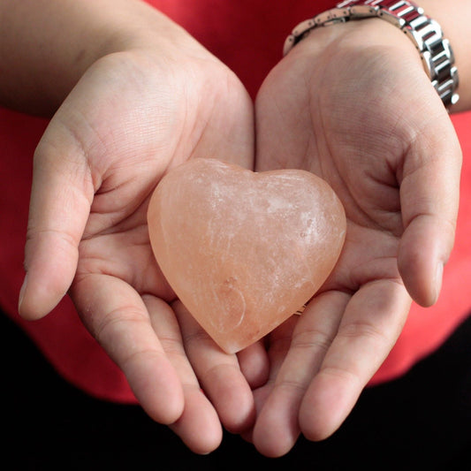 Manos sosteniendo un desodorante de sal mineral rosada con forma de corazón, de textura traslúcida y natural.