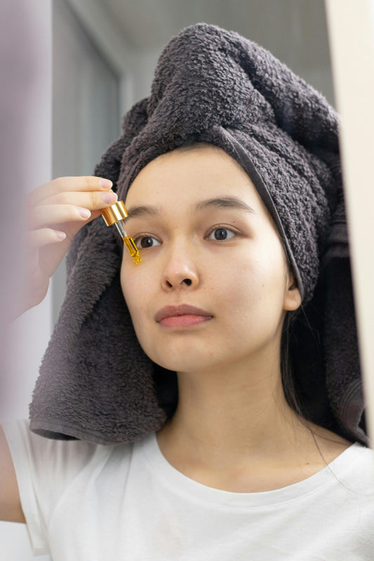 Young woman applying eye serum with dropper after shower