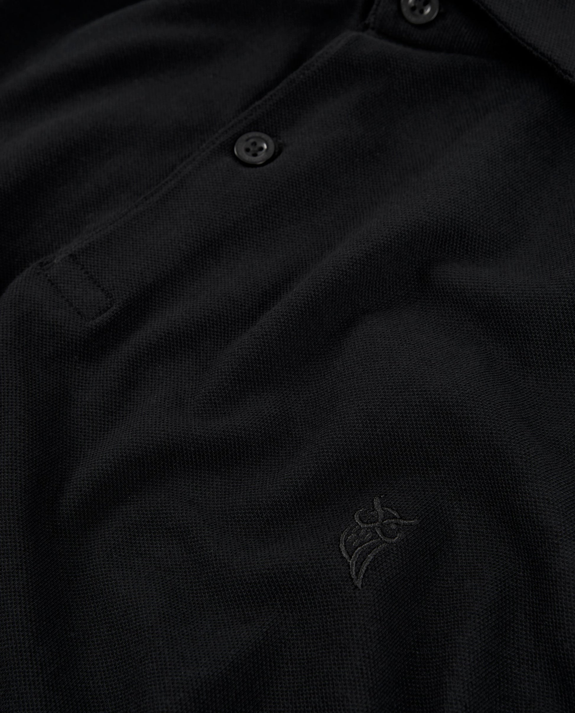 Polo negro de algodón con botones y logo bordado, estilo clásico y elegante.