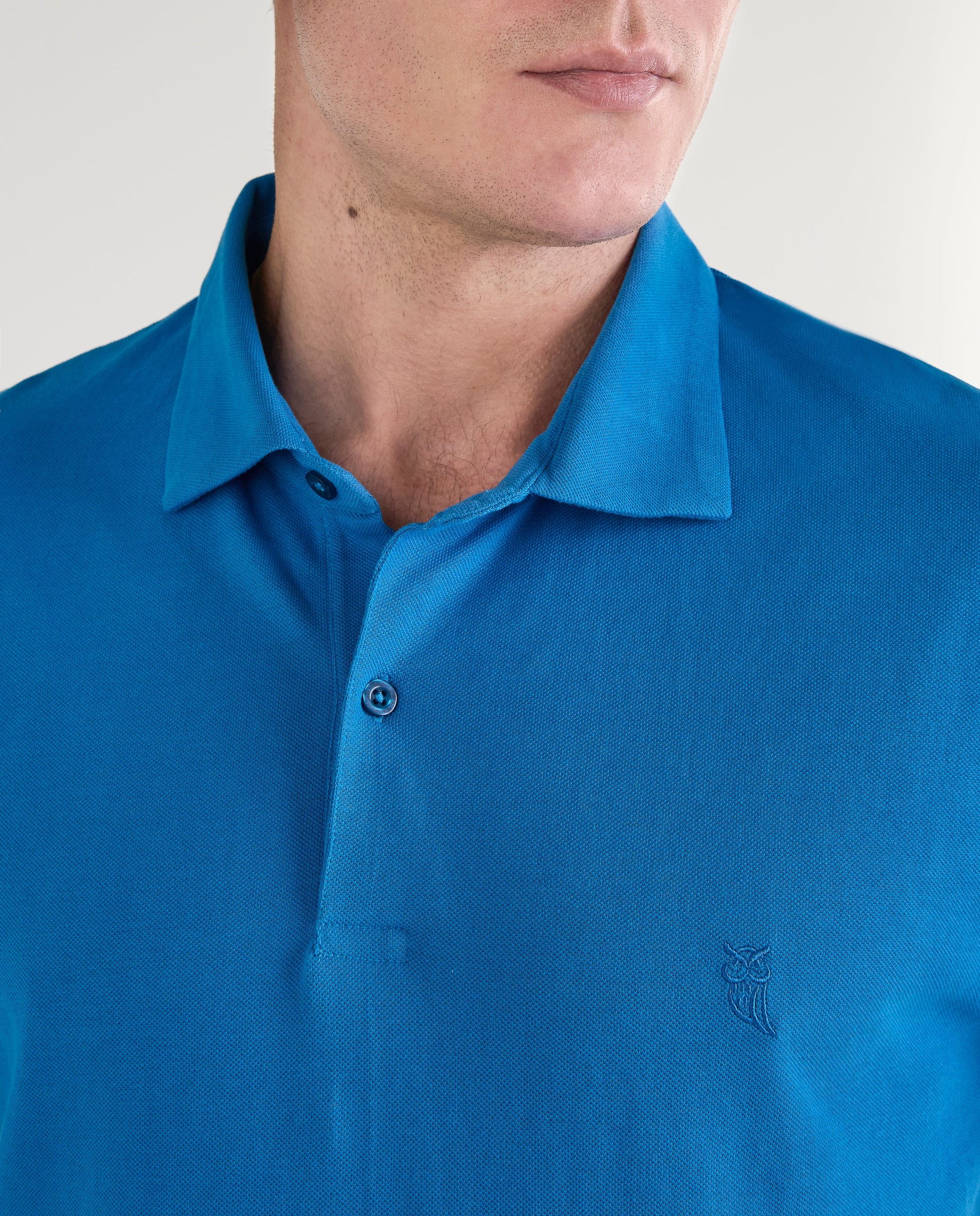 Polo azul vibrante de algodón para hombre con logo bordado de búho en el pecho. Elegantemente casual.