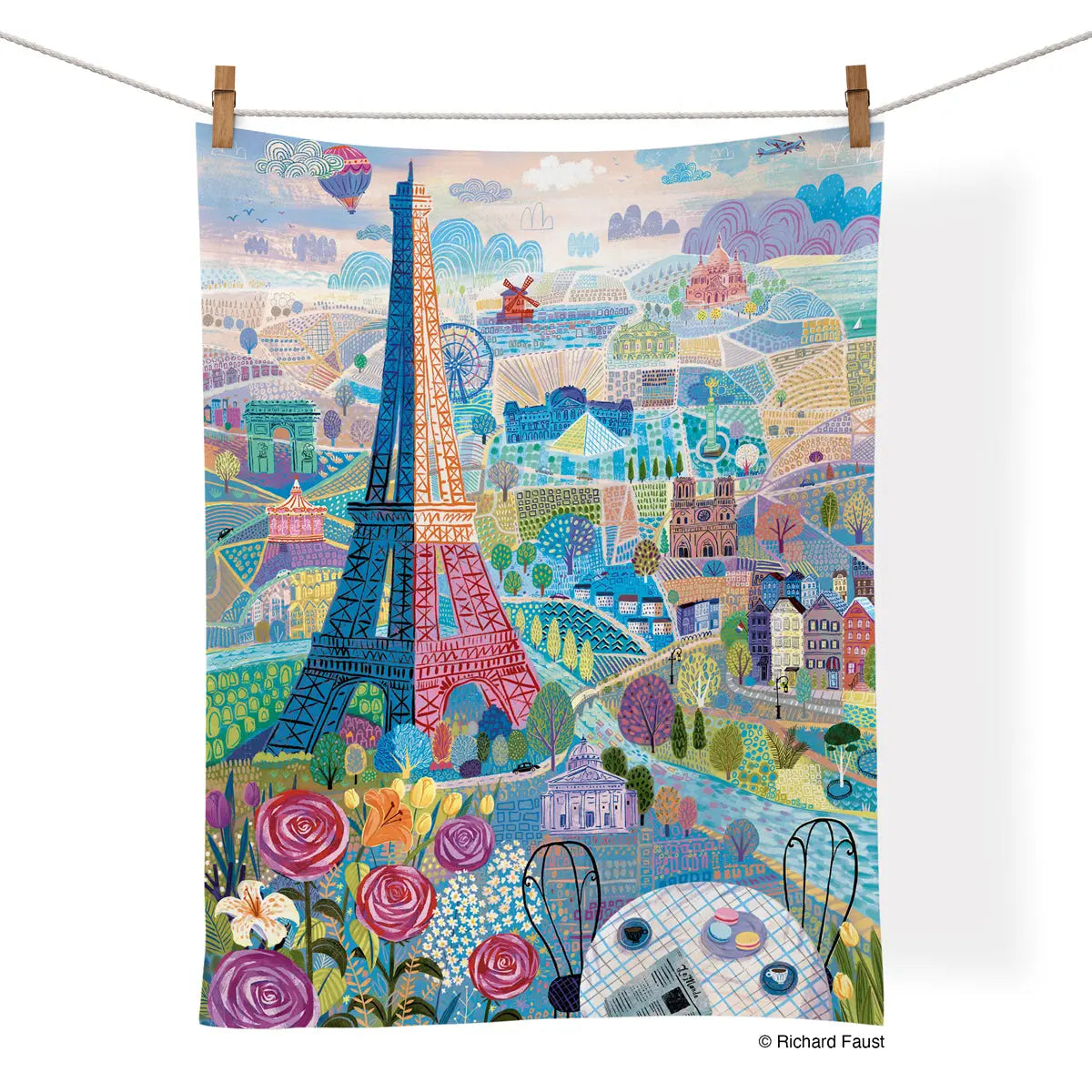 Cotton tea towel hanging on a line, featuring a whimsical, colorful illustration of Parisian landmarks and florals.