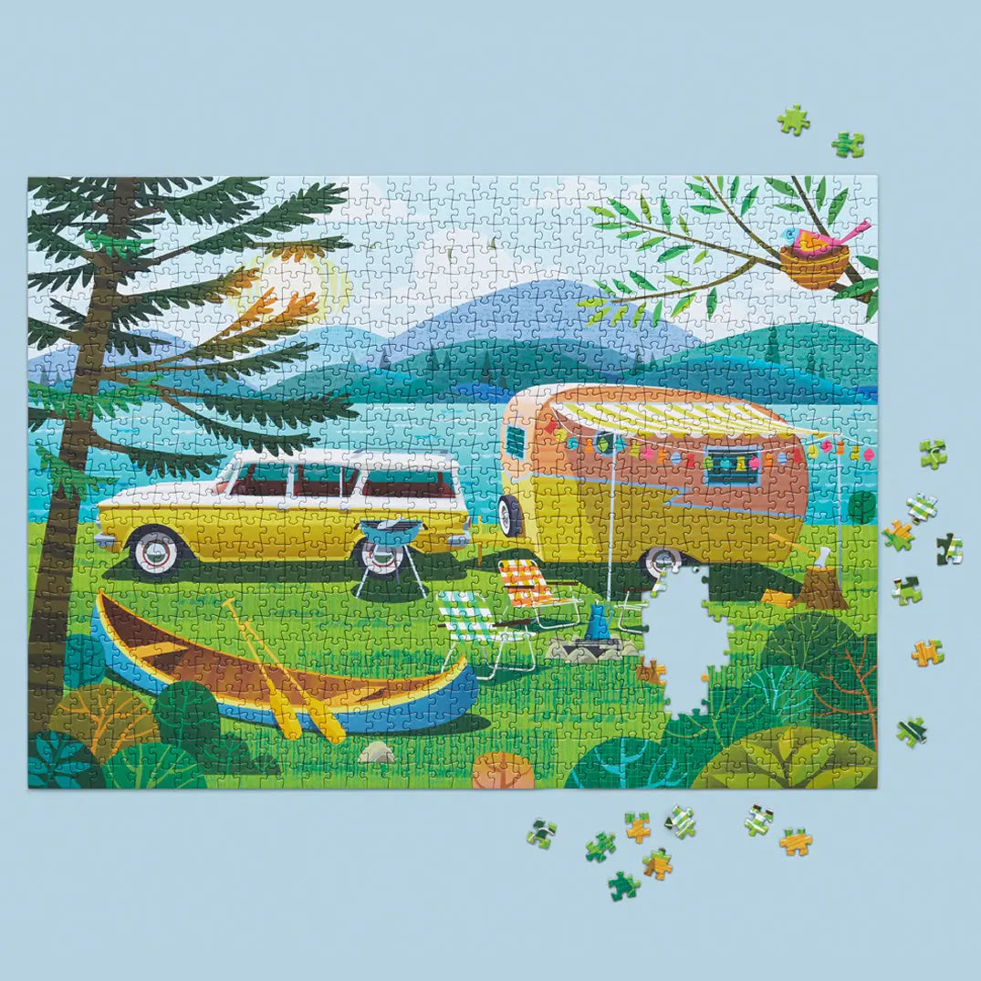 Colorful 1000-piece puzzle showing a vintage car and camper parked by a lake, with a canoe and camping gear.