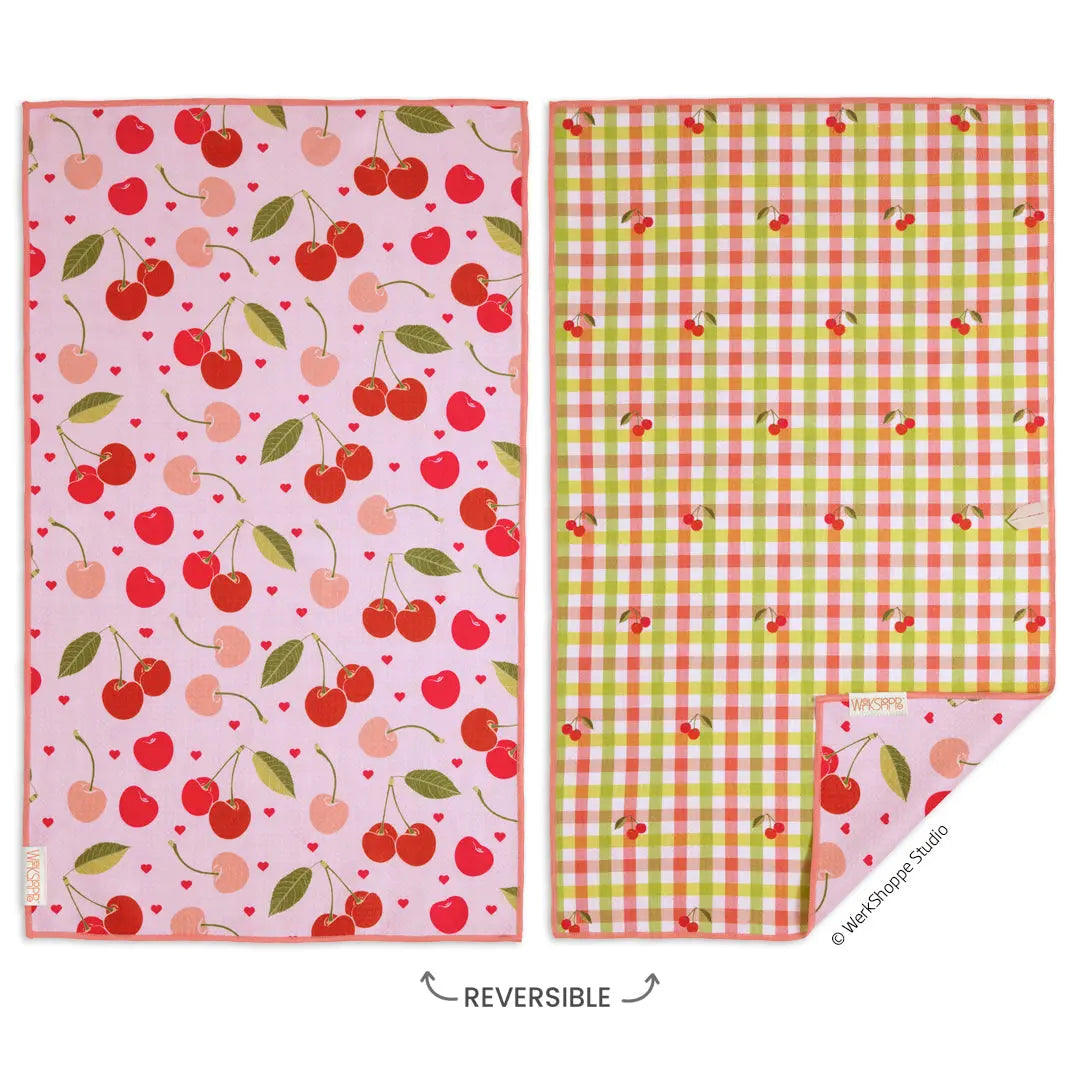Two rectangular microfiber towels. Left: pink with red cherries and hearts. Right: green and orange gingham with cherries.