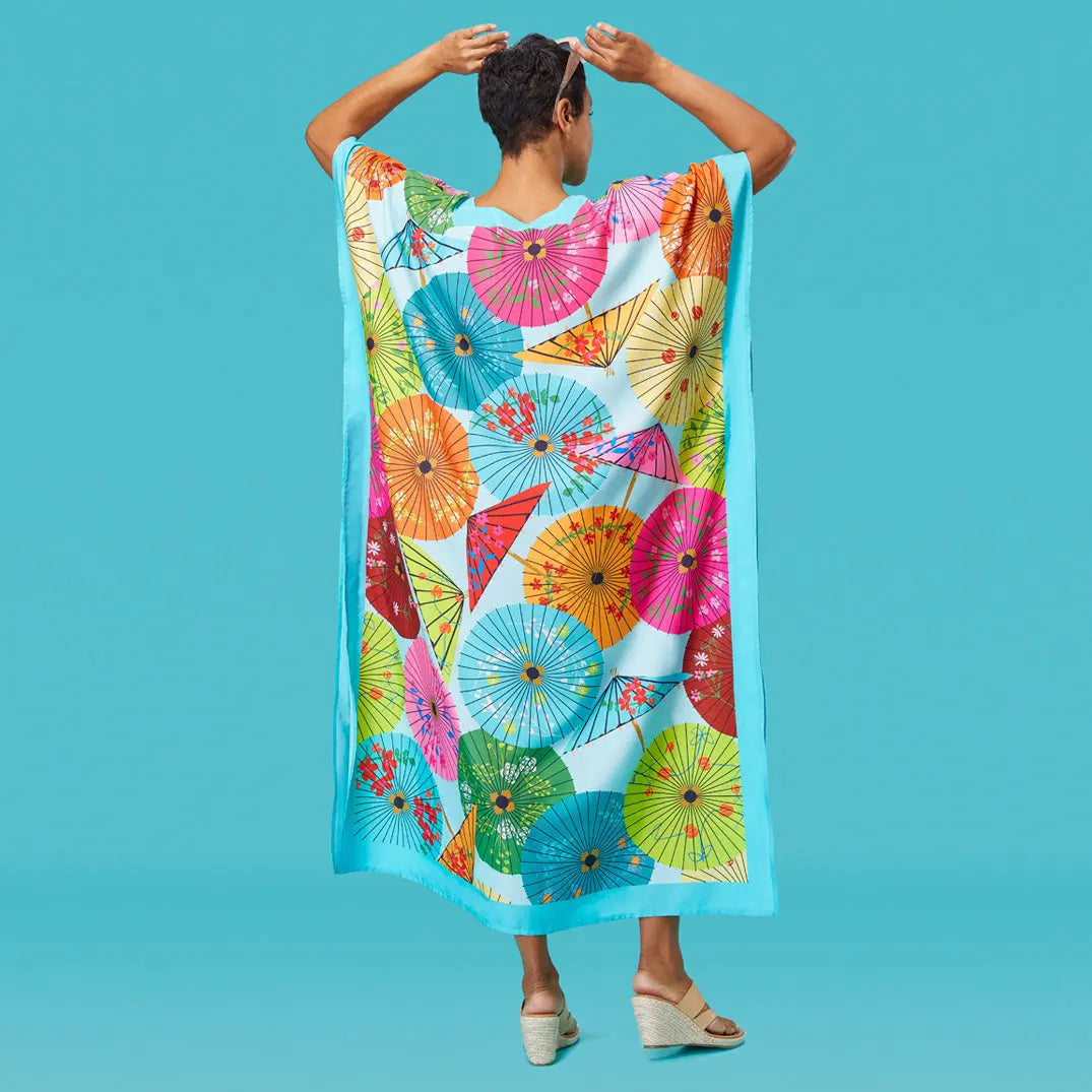 Person wearing a light blue caftan with a colorful pattern of parasols, against a matching solid blue background.