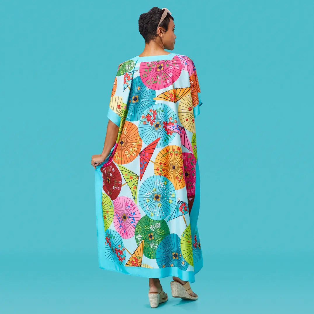 A model wearing a light blue, floor-length caftan patterned with colorful, vibrant paper parasols.