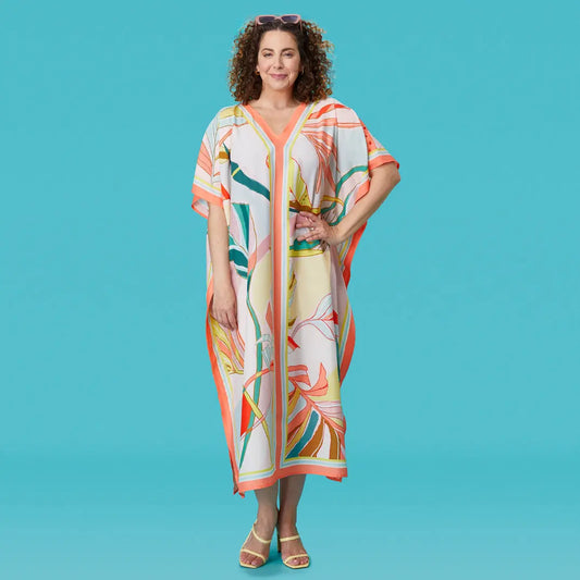 Woman wearing a loose-fitting, V-neck caftan with a colorful tropical leaf print in coral, green, and yellow accents.